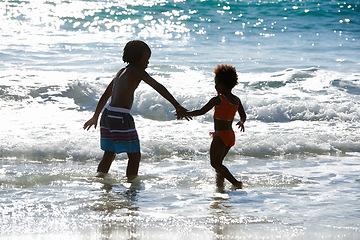 Image showing Back, beach and kids holding hands in water at sea, love and together on summer holiday. African children, ocean and rear view of siblings, brother and sister on vacation, travel and family outdoor