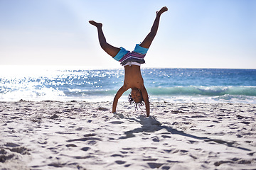 Image showing Cartwheel, happy and child on beach for fun, playing and relax on holiday, vacation and weekend. Travel, nature and young African boy do handstand on sand for freedom, adventure and enjoy childhood