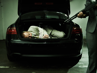 Image showing Man in trunk of car, kidnapping and gun with mafia, danger and violence in basement garage. Crime, human trafficking and scared person tied with rope parking lot with gangster, robbery and terror.