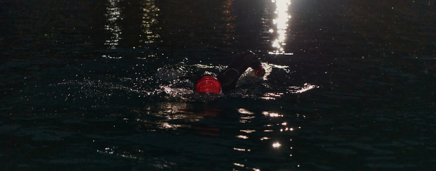 Image showing A determined professional triathlete undergoes rigorous night time training in cold waters, showcasing dedication and resilience in preparation for an upcoming triathlon swim competition