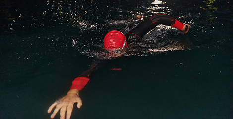 Image showing A determined professional triathlete undergoes rigorous night time training in cold waters, showcasing dedication and resilience in preparation for an upcoming triathlon swim competition