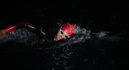 Image showing A determined professional triathlete undergoes rigorous night time training in cold waters, showcasing dedication and resilience in preparation for an upcoming triathlon swim competition