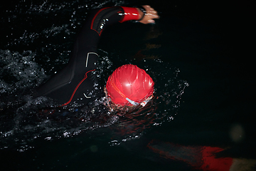 Image showing A determined professional triathlete undergoes rigorous night time training in cold waters, showcasing dedication and resilience in preparation for an upcoming triathlon swim competition