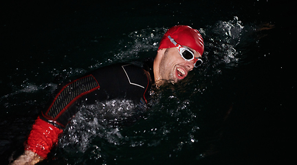 Image showing A determined professional triathlete undergoes rigorous night time training in cold waters, showcasing dedication and resilience in preparation for an upcoming triathlon swim competition