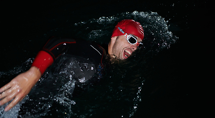 Image showing A determined professional triathlete undergoes rigorous night time training in cold waters, showcasing dedication and resilience in preparation for an upcoming triathlon swim competition