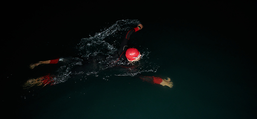 Image showing A determined professional triathlete undergoes rigorous night time training in cold waters, showcasing dedication and resilience in preparation for an upcoming triathlon swim competition