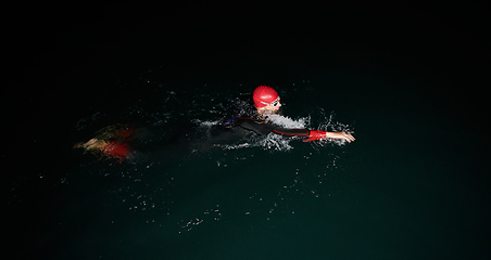 Image showing A determined professional triathlete undergoes rigorous night time training in cold waters, showcasing dedication and resilience in preparation for an upcoming triathlon swim competition