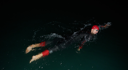 Image showing A determined professional triathlete undergoes rigorous night time training in cold waters, showcasing dedication and resilience in preparation for an upcoming triathlon swim competition