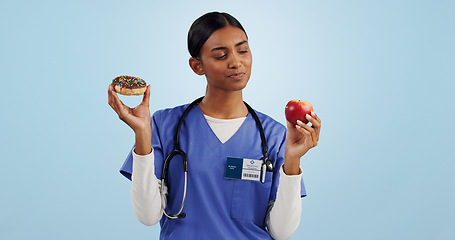 Image showing Apple, donut and nurse in studio with choice for healthy eating, diet and detox on blue background. Thinking, healthcare and Indian woman with dessert, fruit and cake for decision, option and balance