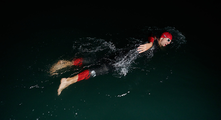 Image showing A determined professional triathlete undergoes rigorous night time training in cold waters, showcasing dedication and resilience in preparation for an upcoming triathlon swim competition