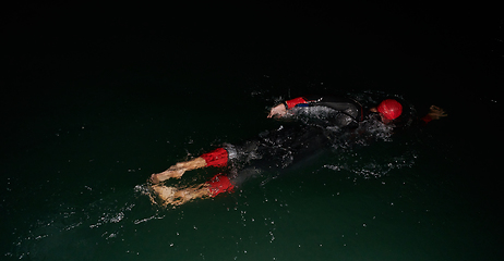 Image showing A determined professional triathlete undergoes rigorous night time training in cold waters, showcasing dedication and resilience in preparation for an upcoming triathlon swim competition