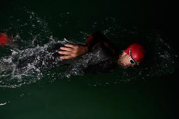 Image showing A determined professional triathlete undergoes rigorous night time training in cold waters, showcasing dedication and resilience in preparation for an upcoming triathlon swim competition