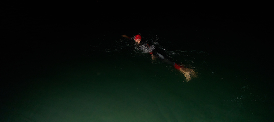 Image showing A determined professional triathlete undergoes rigorous night time training in cold waters, showcasing dedication and resilience in preparation for an upcoming triathlon swim competition