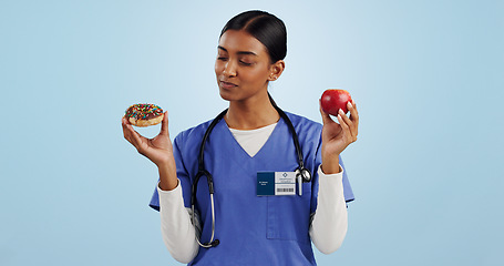 Image showing Apple, donut and doctor in studio with choice for healthy eating, diet and detox on blue background. Thinking, healthcare and Indian woman with candy, fruit and cake for decision, diabetes or balance