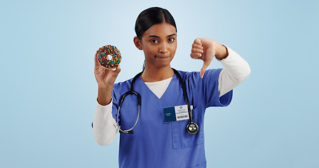 Image showing Woman, portrait and doctor with thumbs down, donut and bad review for diet on a blue studio background. Female person rejection, emoji or sign with chocolate dessert, diabetes and high blood sugar