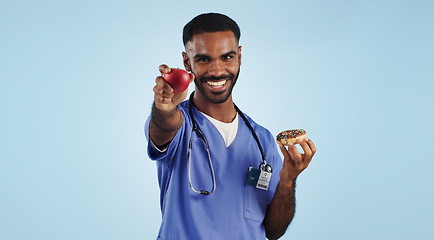 Image showing Happy man, doctor and apple with donut for diet or healthy eating by a blue studio background. Portrait of male person or medical nurse smile with organic fruit and chocolate dessert for choice