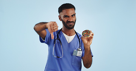 Image showing Man, portrait and doctor with thumbs down, donut or bad review for diet against a blue studio background. Brazilian person or medical nurse rejection, no emoji or sign for chocolate dessert on mockup