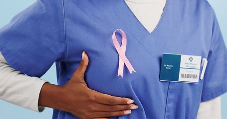 Image showing Woman, doctor and chest in closeup with breast cancer ribbon for promotion, awareness or solidarity. Female medic, hand and fabric sign for kindness, empathy and wellness in studio by blue background