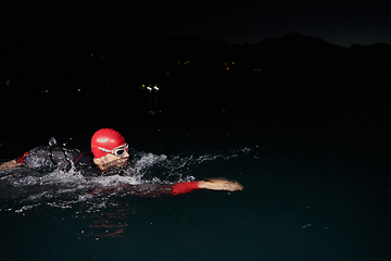 Image showing A determined professional triathlete undergoes rigorous night time training in cold waters, showcasing dedication and resilience in preparation for an upcoming triathlon swim competition