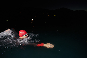 Image showing A determined professional triathlete undergoes rigorous night time training in cold waters, showcasing dedication and resilience in preparation for an upcoming triathlon swim competition