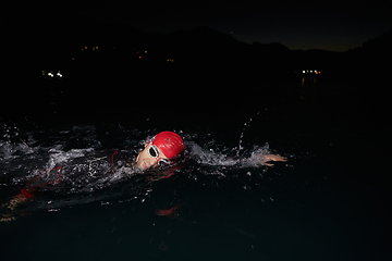 Image showing A determined professional triathlete undergoes rigorous night time training in cold waters, showcasing dedication and resilience in preparation for an upcoming triathlon swim competition