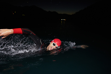 Image showing A determined professional triathlete undergoes rigorous night time training in cold waters, showcasing dedication and resilience in preparation for an upcoming triathlon swim competition