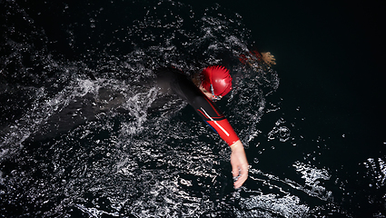 Image showing A determined professional triathlete undergoes rigorous night time training in cold waters, showcasing dedication and resilience in preparation for an upcoming triathlon swim competition