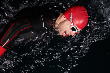 Image showing A determined professional triathlete undergoes rigorous night time training in cold waters, showcasing dedication and resilience in preparation for an upcoming triathlon swim competition