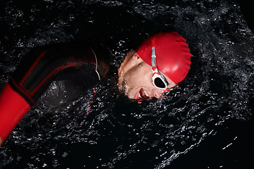 Image showing A determined professional triathlete undergoes rigorous night time training in cold waters, showcasing dedication and resilience in preparation for an upcoming triathlon swim competition