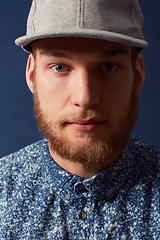 Image showing Man, fashion and face with hat in a studio, denim and trendy isolated on blue background. Irish model with hipster beard, ginger and serious in portrait, stylish and fashionable shirt in headshot