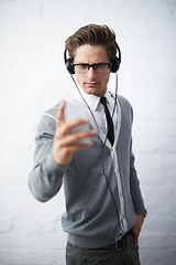 Image showing Business man, headphones and phone with texting, reading and listening to music by wall background. Entrepreneur, person or employee with smartphone, audio streaming subscription and social network