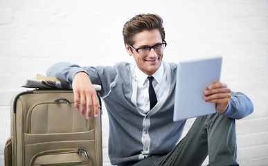 Image showing Business man, reading or suitcase with tablet, floor and smile with app, flight or travel by wall background. Entrepreneur, person or touchscreen on social media, bag or check booking for immigration