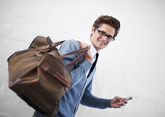 Image showing Business man, bag and phone in portrait by wall background with click for booking app, schedule and travel. Entrepreneur, employee and smartphone for smile, reading and scroll on website for flight