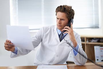 Image showing Document, phone call and man doctor in his office for telehealth consultation at hospital. Confused, professional and young male healthcare worker on mobile discussion with landline in medical clinic