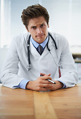 Image showing Serious, confused and portrait of doctor in his office for medical consultation at hospital. Doubt, thinking and professional young male healthcare worker with stethoscope by desk at medicare clinic.