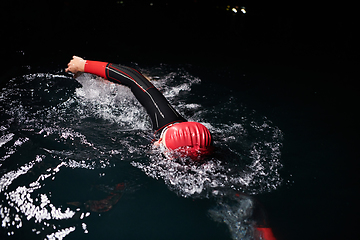 Image showing A determined professional triathlete undergoes rigorous night time training in cold waters, showcasing dedication and resilience in preparation for an upcoming triathlon swim competition