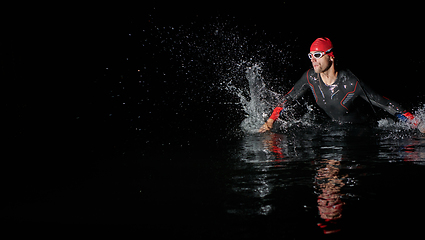 Image showing A determined professional triathlete undergoes rigorous night time training in cold waters, showcasing dedication and resilience in preparation for an upcoming triathlon swim competition