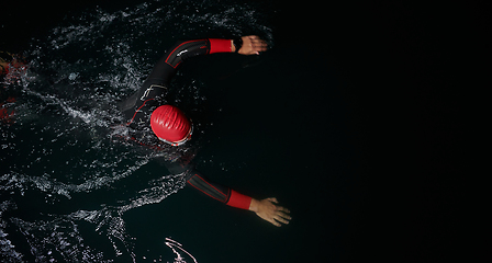 Image showing A determined professional triathlete undergoes rigorous night time training in cold waters, showcasing dedication and resilience in preparation for an upcoming triathlon swim competition