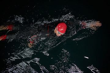 Image showing A determined professional triathlete undergoes rigorous night time training in cold waters, showcasing dedication and resilience in preparation for an upcoming triathlon swim competition