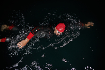 Image showing A determined professional triathlete undergoes rigorous night time training in cold waters, showcasing dedication and resilience in preparation for an upcoming triathlon swim competition