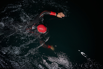 Image showing A determined professional triathlete undergoes rigorous night time training in cold waters, showcasing dedication and resilience in preparation for an upcoming triathlon swim competition