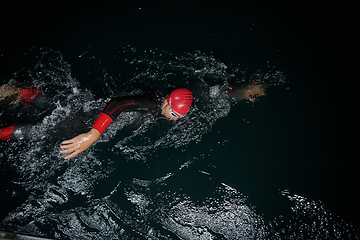 Image showing A determined professional triathlete undergoes rigorous night time training in cold waters, showcasing dedication and resilience in preparation for an upcoming triathlon swim competition