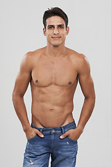 Image showing Man, portrait and confident in studio for fashion, smiling and bodybuilder in jeans for style. Male person, shirtless and fitness or muscle progress, face and body care or wellness by gray background