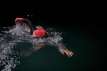 Image showing A determined professional triathlete undergoes rigorous night time training in cold waters, showcasing dedication and resilience in preparation for an upcoming triathlon swim competition