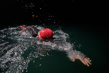 Image showing A determined professional triathlete undergoes rigorous night time training in cold waters, showcasing dedication and resilience in preparation for an upcoming triathlon swim competition