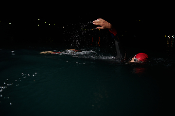 Image showing A determined professional triathlete undergoes rigorous night time training in cold waters, showcasing dedication and resilience in preparation for an upcoming triathlon swim competition