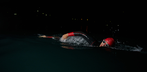 Image showing A determined professional triathlete undergoes rigorous night time training in cold waters, showcasing dedication and resilience in preparation for an upcoming triathlon swim competition