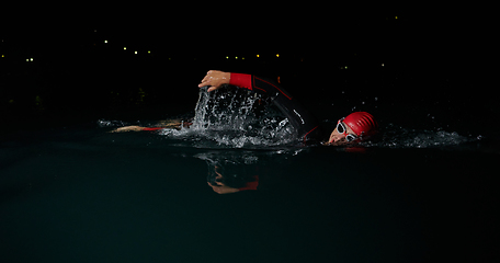 Image showing A determined professional triathlete undergoes rigorous night time training in cold waters, showcasing dedication and resilience in preparation for an upcoming triathlon swim competition