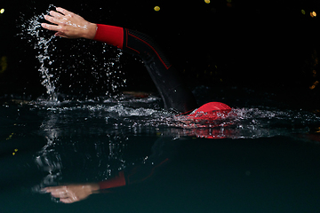 Image showing A determined professional triathlete undergoes rigorous night time training in cold waters, showcasing dedication and resilience in preparation for an upcoming triathlon swim competition