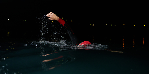 Image showing A determined professional triathlete undergoes rigorous night time training in cold waters, showcasing dedication and resilience in preparation for an upcoming triathlon swim competition